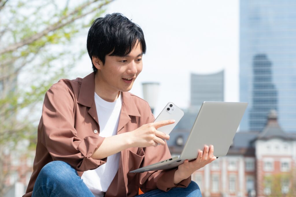 屋外でテザリングを使ってノートパソコンを開く男性